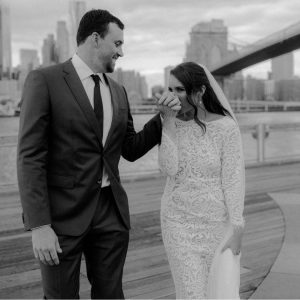 Bride kissing grooms hand in front of Brooklyn Bridge