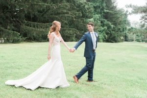 bride & groom holding hands on green field