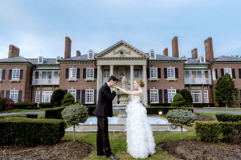 Groom kissing brides hand in front of Glencove Mansion