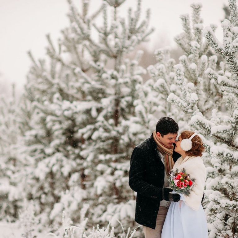 Bride and groom kissing with snow capped trees behind them