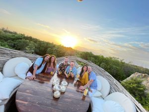 3 couples sitting at dinner with the sunset and trees in the background in Tulum Mexico